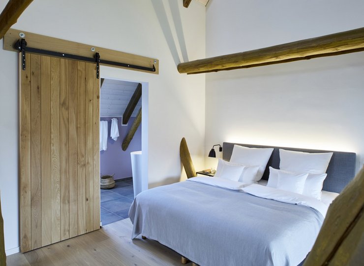 Ein Zimmer in einem Boarding House in Wolfsburg. Die Wände sind weiß gestrichen, die Türen, der Fußboden und die offenliegenden Dachstreben sind aus Holz.